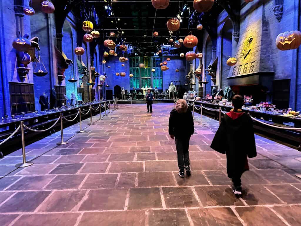 Two boys walk into the Great Hall film set from the Harry Potter films. There are pumpkins floating in the air.