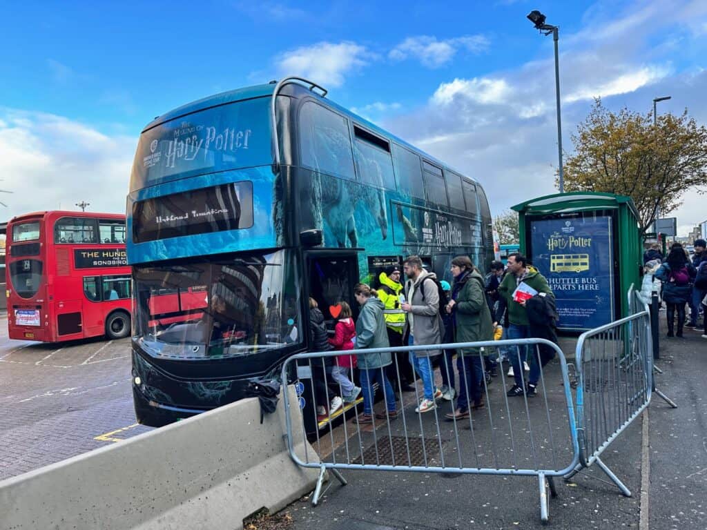 People getting on double decker shuttle bus for Harry Potter Studio Tour in London. You can also see a red double decker bus on the left.
