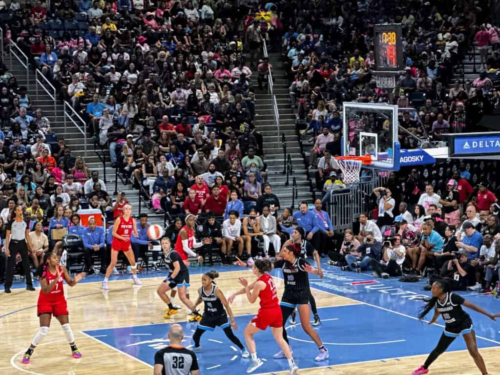 WNBA players from Indiana Fever and Chicago Sky on the court at Wintrust Arena in Chicago in front of packed stands.