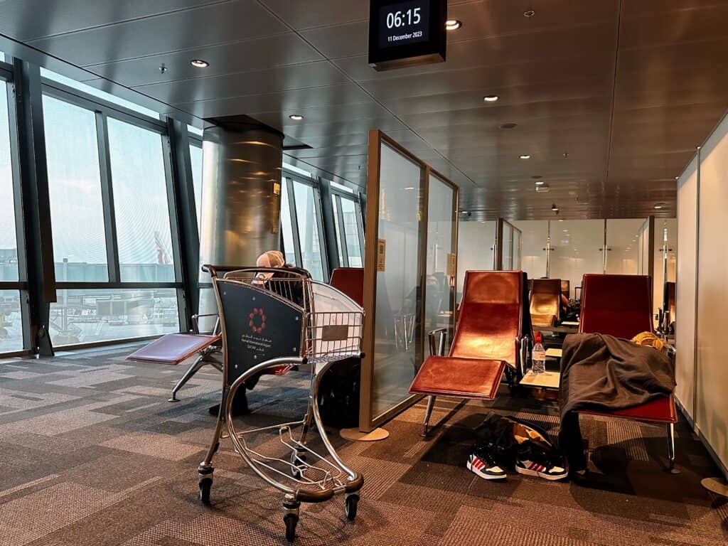 Child sleeps in a lounge chair at Doha airport. Metal luggage cart to left.