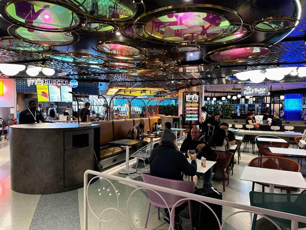 Colorful foodcourt with restaurants and dining table area. Some people are eating at the tables.