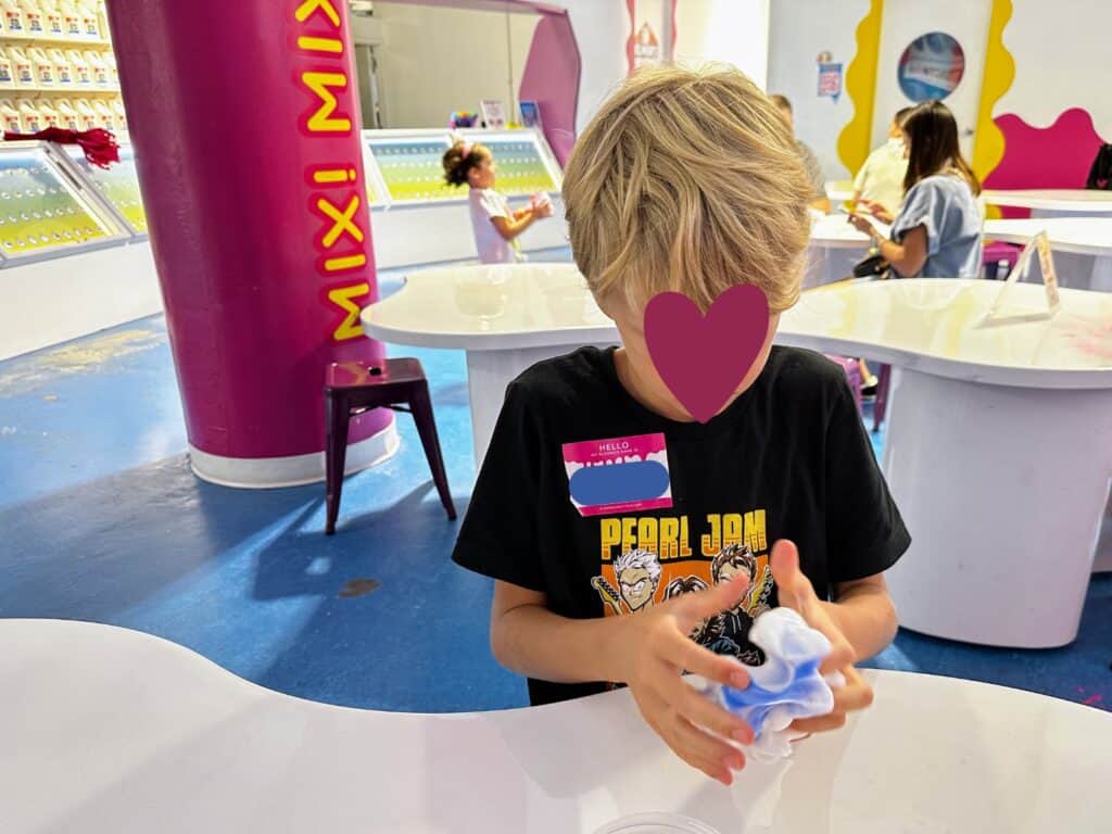 Boy mixes personalized slime at a white table at the Sloomoo Institute in Chicago, Illinois.