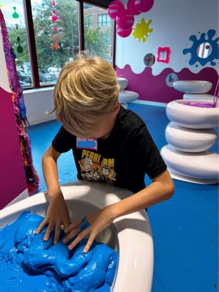 Boy puts hands in tub of blue slime at the Sloomoo Institute in Chicago, Illinois.
