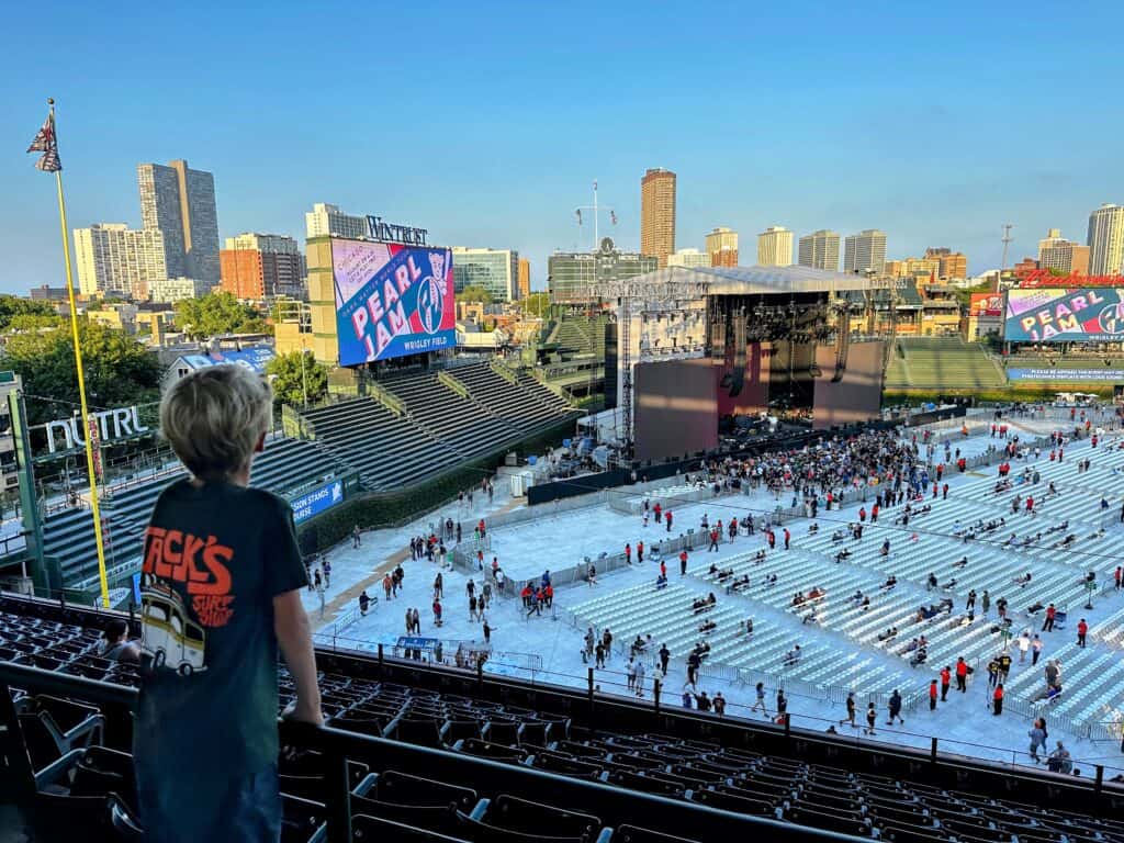 Boy stands in upper level of Wrigley Field in Chicago looking out over the concert stage for a Pearl Jam concert. Chicago skyline in the background.