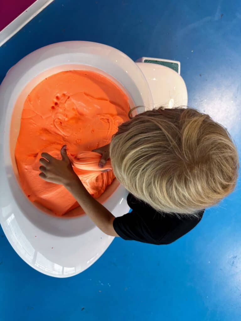 Boy plays in large vat of orange slime at the Sloomoo Institute in Chicago, Illinois.