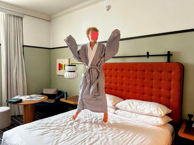 Boy in large grey robe jumps on the bed in a hotel room in L7 by Lotte in Chicago, Illinois.
