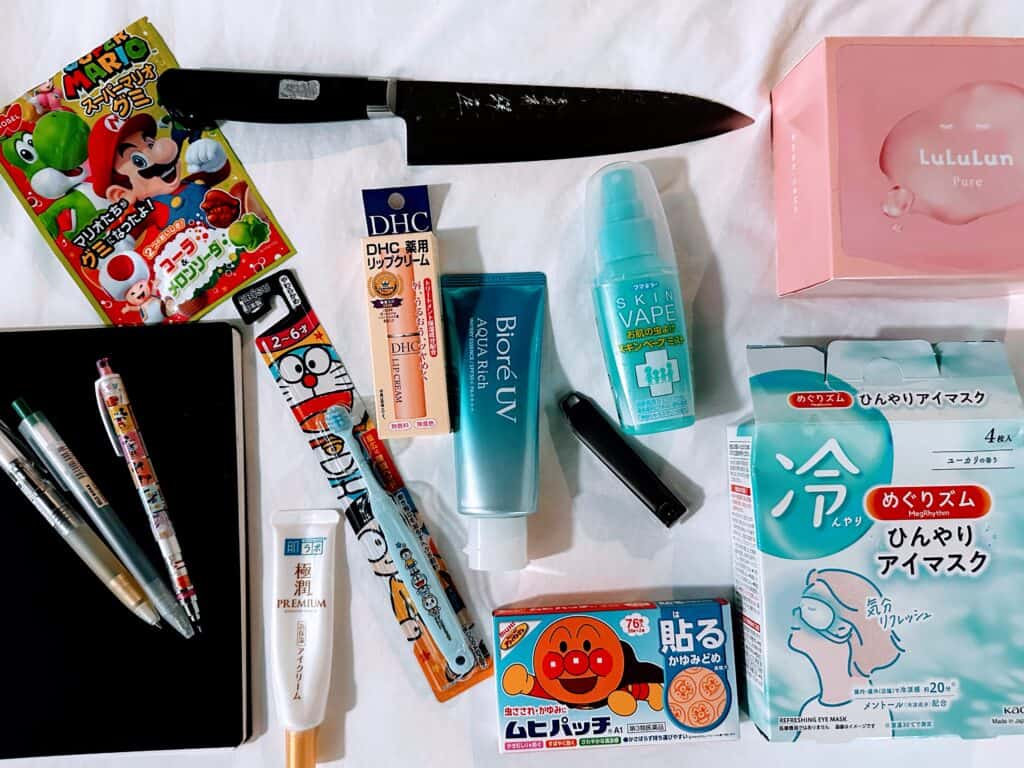 Souvenirs from Japan (including a knife, face masks, nail clippers, sunscreen, pens, and a notebook) on a white sheet.