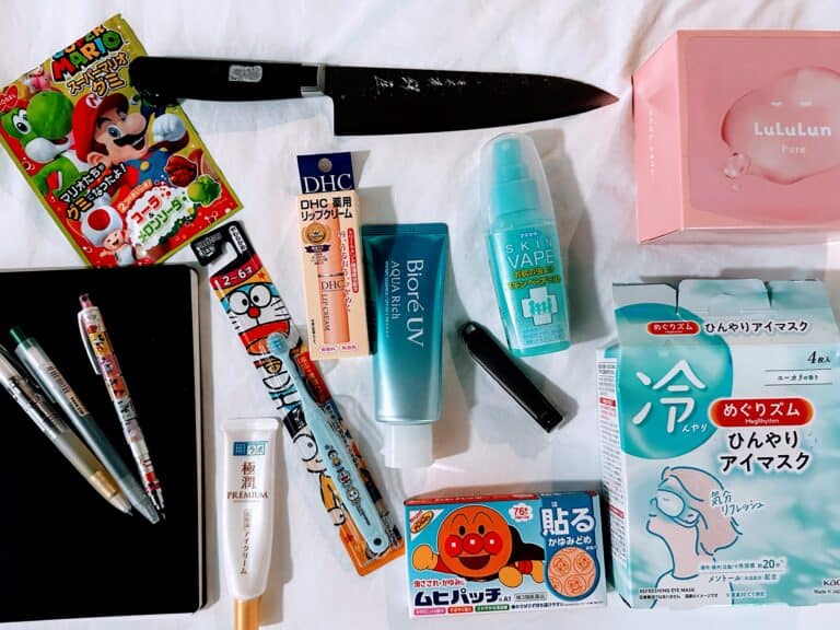 Souvenirs from Japan (including a knife, face masks, nail clippers, sunscreen, pens, and a notebook) on a white sheet.