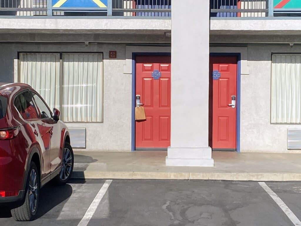 Red doors on the first floor of the Castle Inn in Anaheim, California. Parking spaces in front of the doors and red car parked on left.