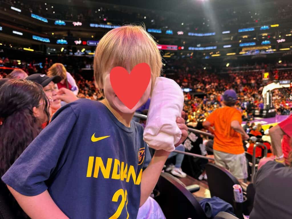 Boy holds up a t-shirt that was thrown from the court into the stands at a Phoenix Mercury WNBA game. The stands are full.
