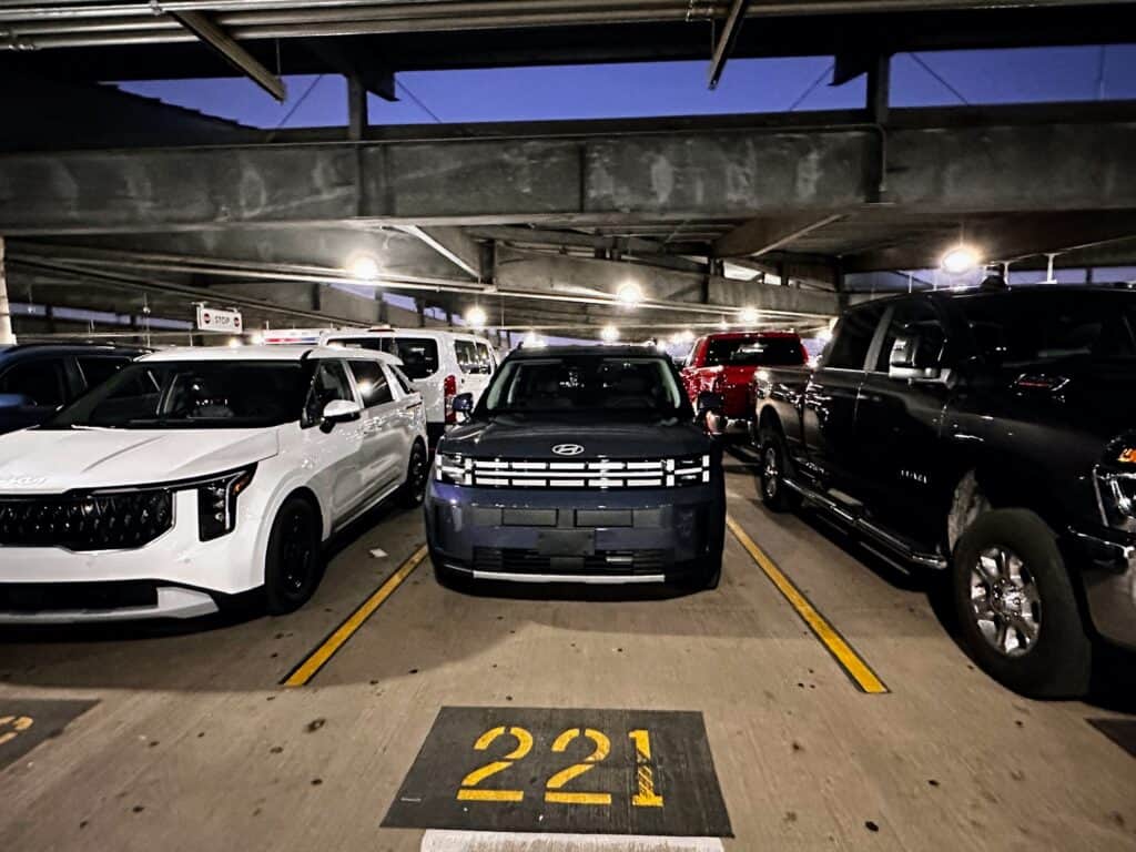 Cars parked in a garage at the PHX airport. Blue SUV in center of photo with parking space 221 marked in front of it.