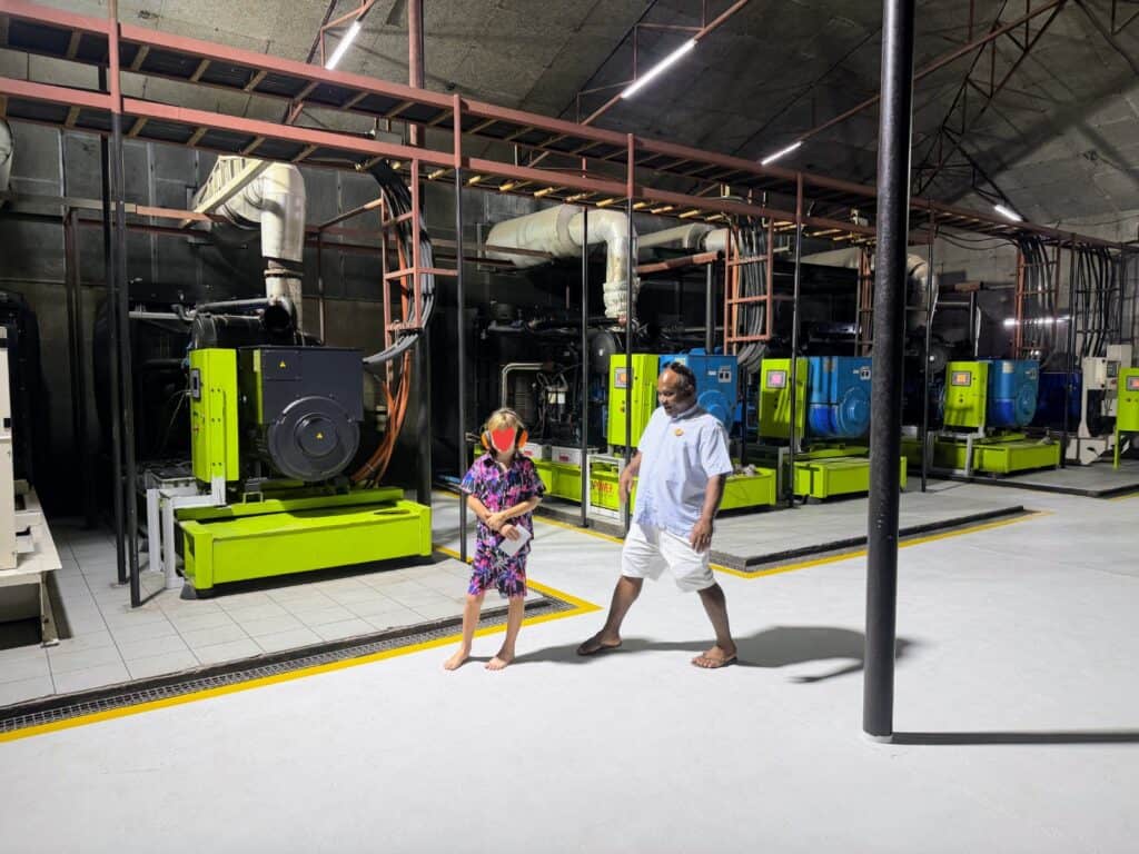 Boy and staff member stand in front of the generators in the generator room at Ayada Maldives.