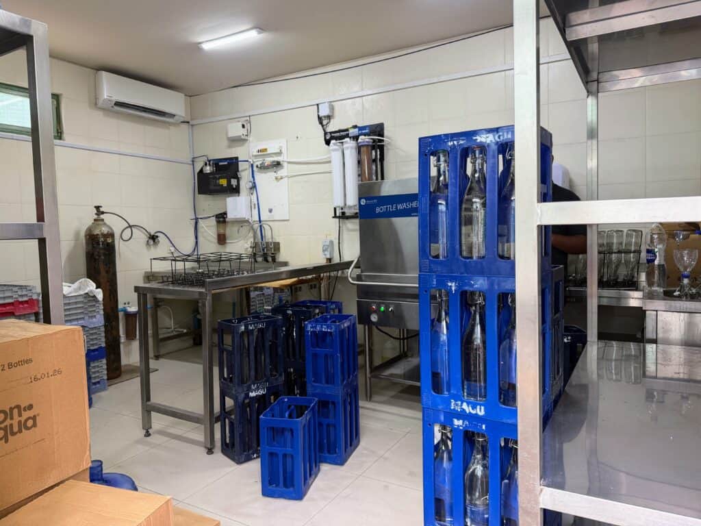 Indoor water bottling room at Ayada Maldives. Blue crates are stacked and hold filled bottles and some are empty and waiting for filled bottles to be placed.