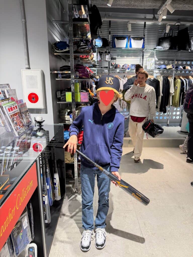 Boy holds baseball bat in front of displays of merchandise at Japan national baseball team store in Tokyo.