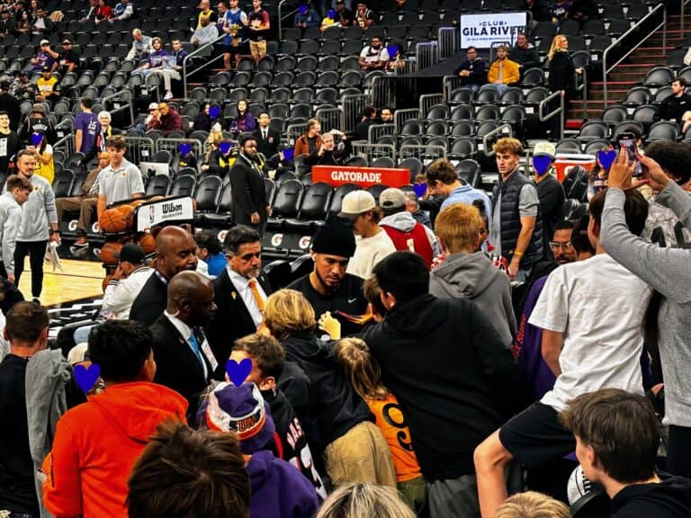 Devin Booker of the Phoenix Suns signs autographs for kids in the stands following his pregame warmup.