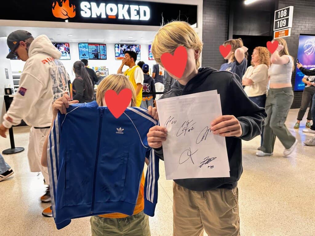 Two blond boys hold up a jacket and piece of paper they got autographed by NBA players at the arena.