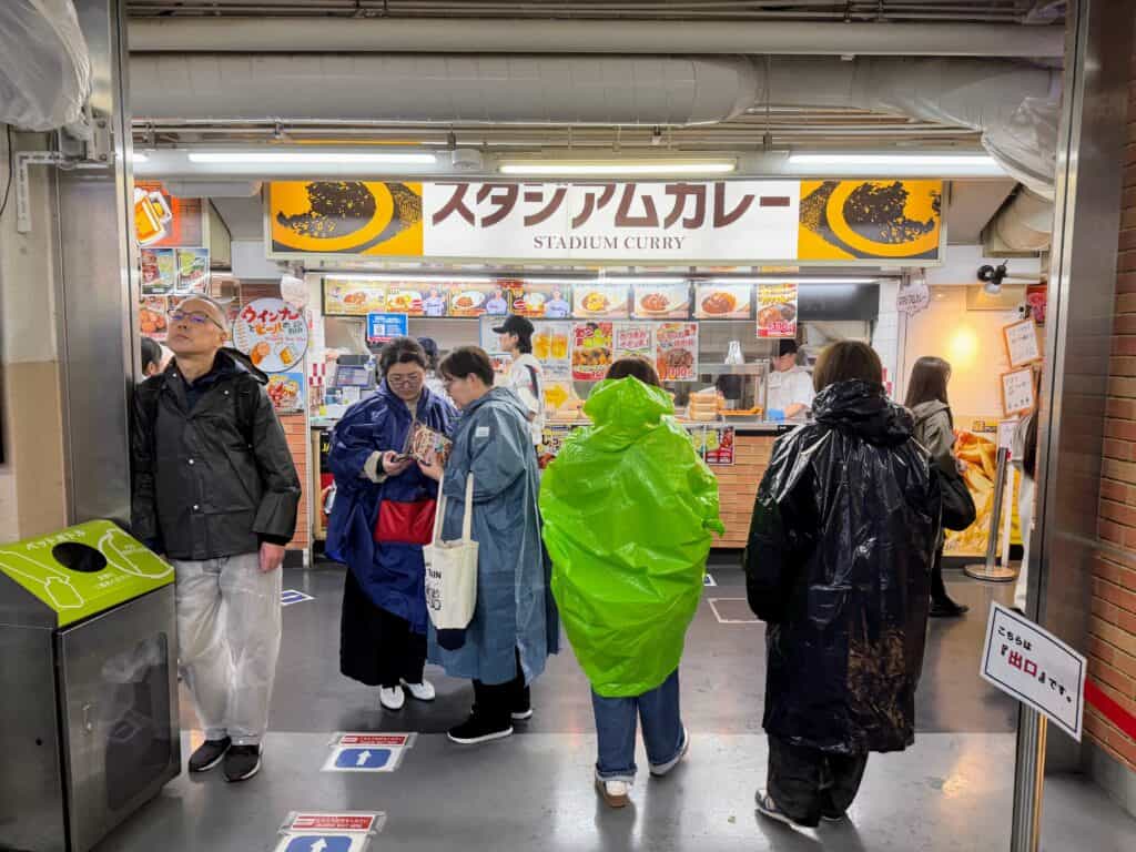 People in rain ponchos walk in front of a curry concession stand inside Meiji Jingu baseball stadium in Tokyo.