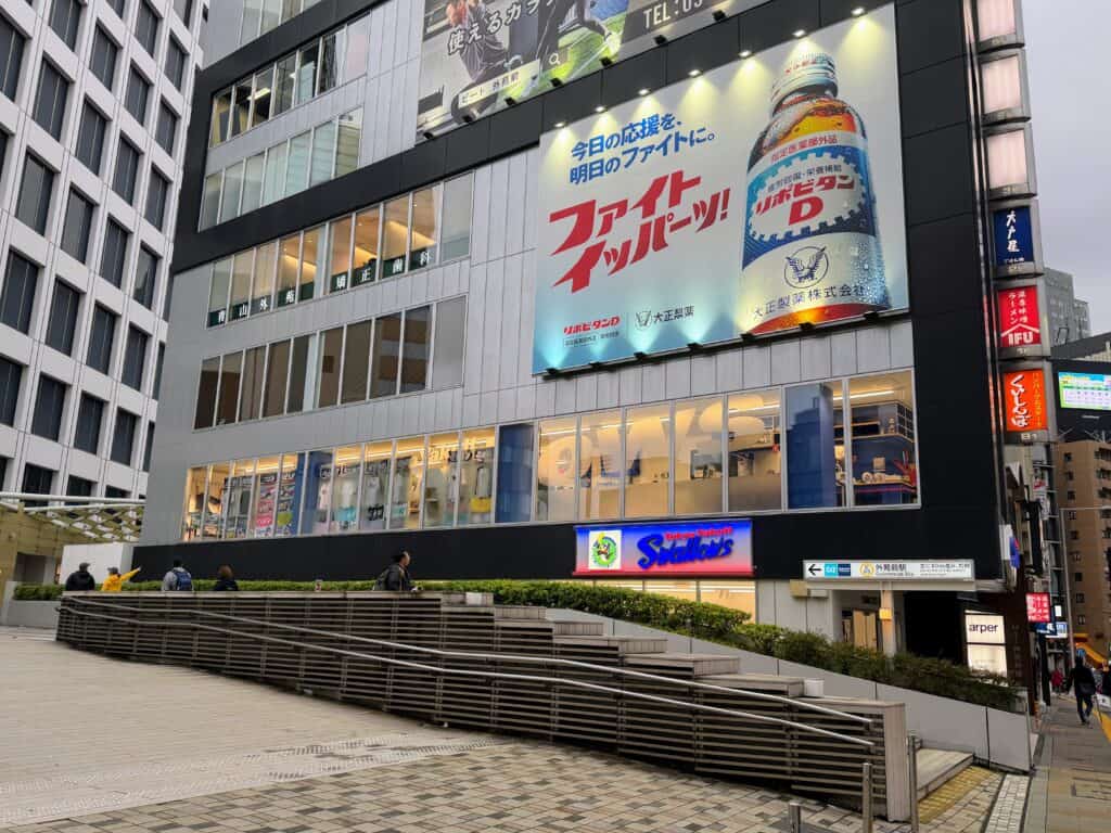 Outside of Yakult Swallows team shop in Tokyo. Multi-story building with glass windows and a billboard.