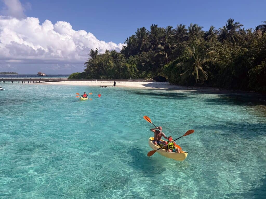 Father and son kayaking in turquoise waters in front of Maldives island resort (Ayada Maldives). Jetty in background.