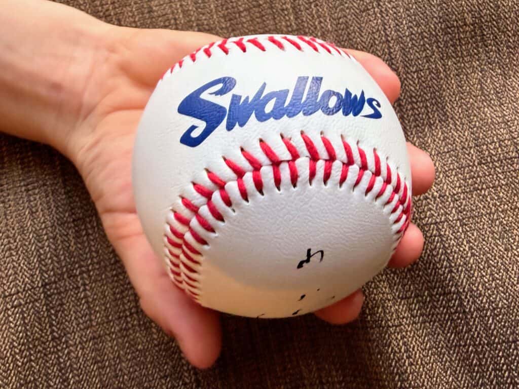 Child's hand holds a baseball with 'Swallows' printed on it (Yakult Swallows of Tokyo).