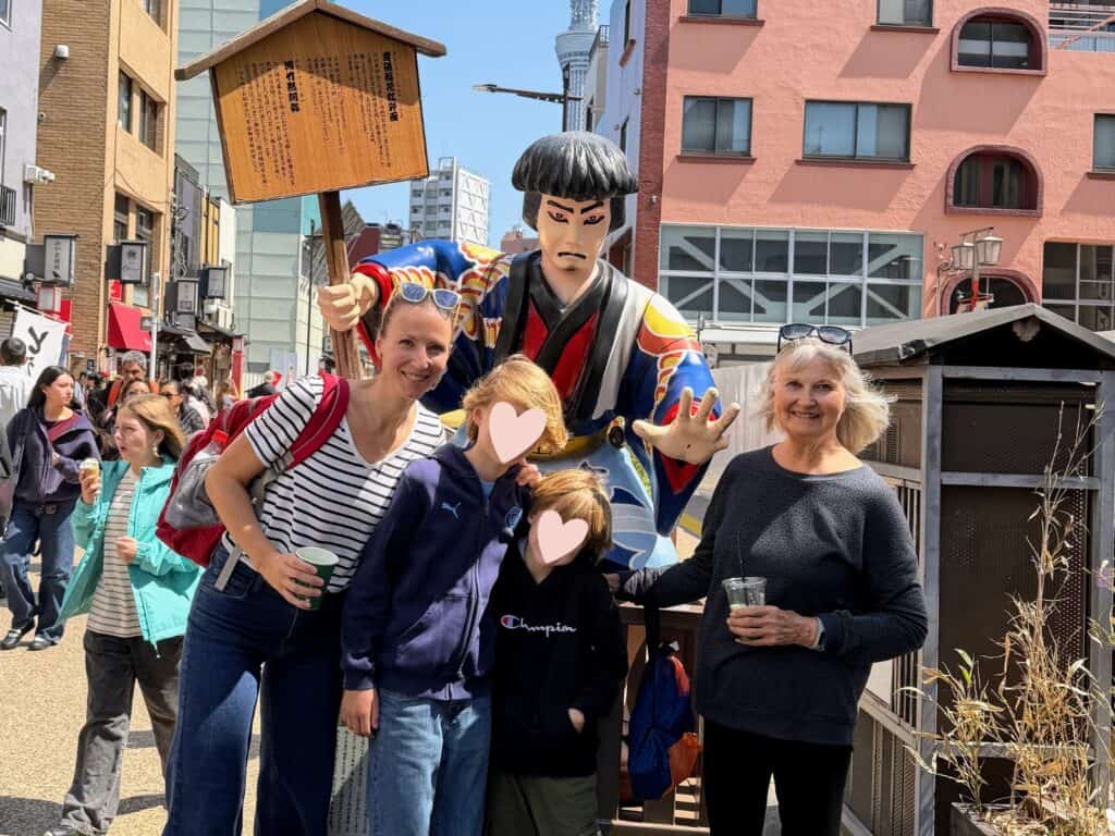 Grandmother, daughter, and grandsons stand with a kabuki statue in Tokyo, Japan.