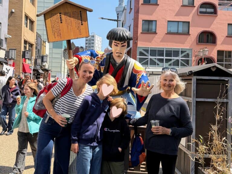 Grandmother, daughter, and grandsons stand with a kabuki statue in Tokyo, Japan.
