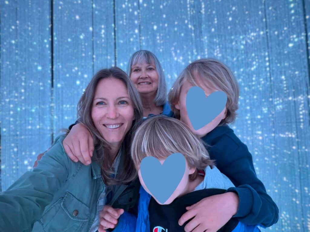 Grandmother, daughter, and grandsons stand in front of sparkly background at Teamlab Planets in Tokyo, Japan.