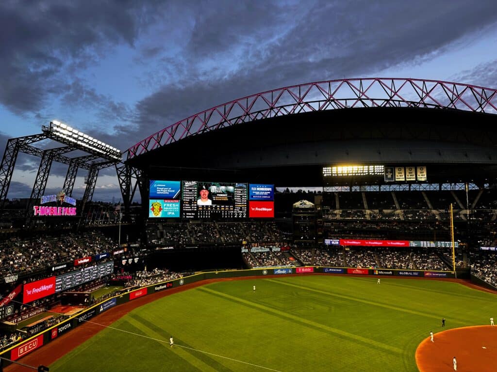Dusk at Seattle Mariners baseball stadium. Players in the field. Stands have fans.