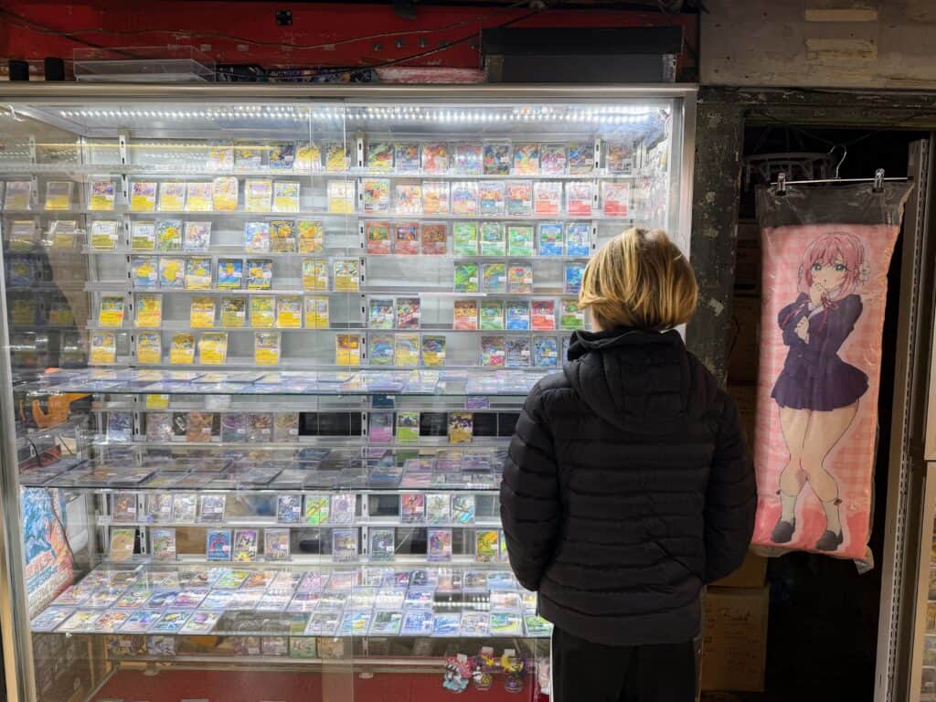 Boy looks at Pokémon cards in a glass display case. He's wearing a black down jacket.