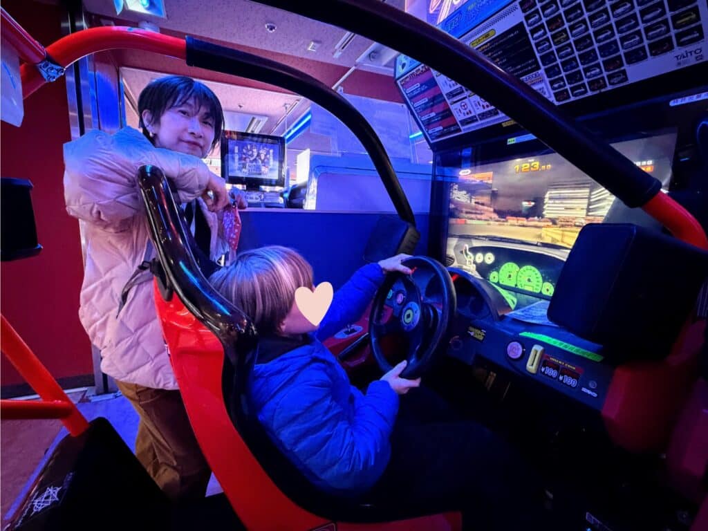 Guide watches boy drive race car arcade game in Tokyo, Japan.