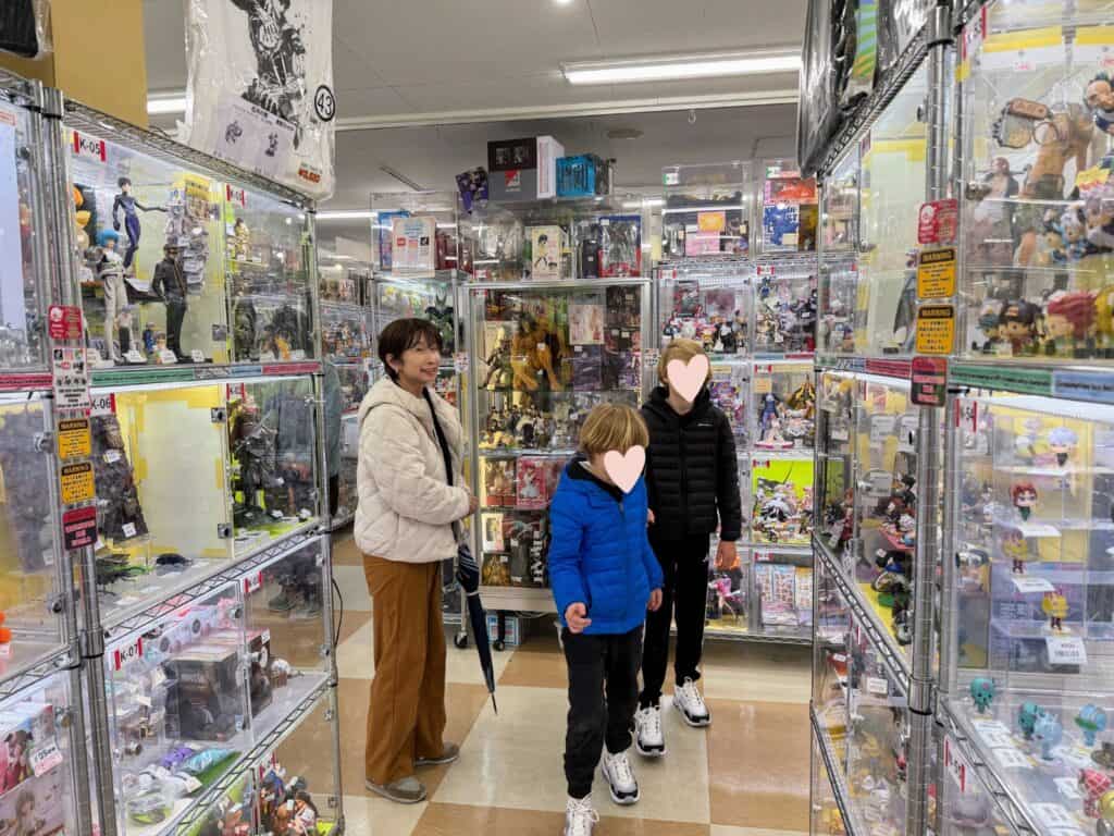 Tour guide with umbrella and two boys stand in anime shop in Tokyo. They are surrounded by glass display cases with anime figures.