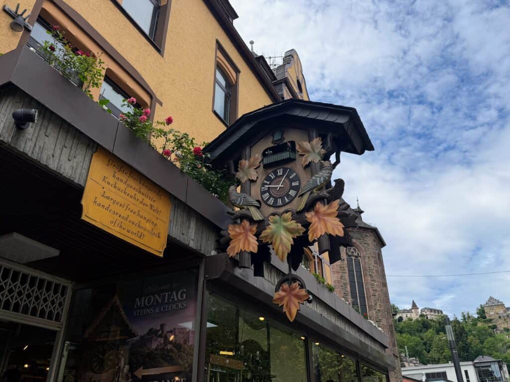 An enormous cuckoo clock hangs from the side of a building. A sign next to it states it's the 'largest freestanding handcarved cuckoo clock in the world!' It's in St. Goar, on the Rhine River in Germany.