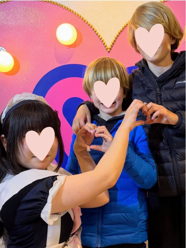 Two boys make hearts with their hands and the hands of a girl dressed as a maid in a maid cafe in Tokyo, Japan.
