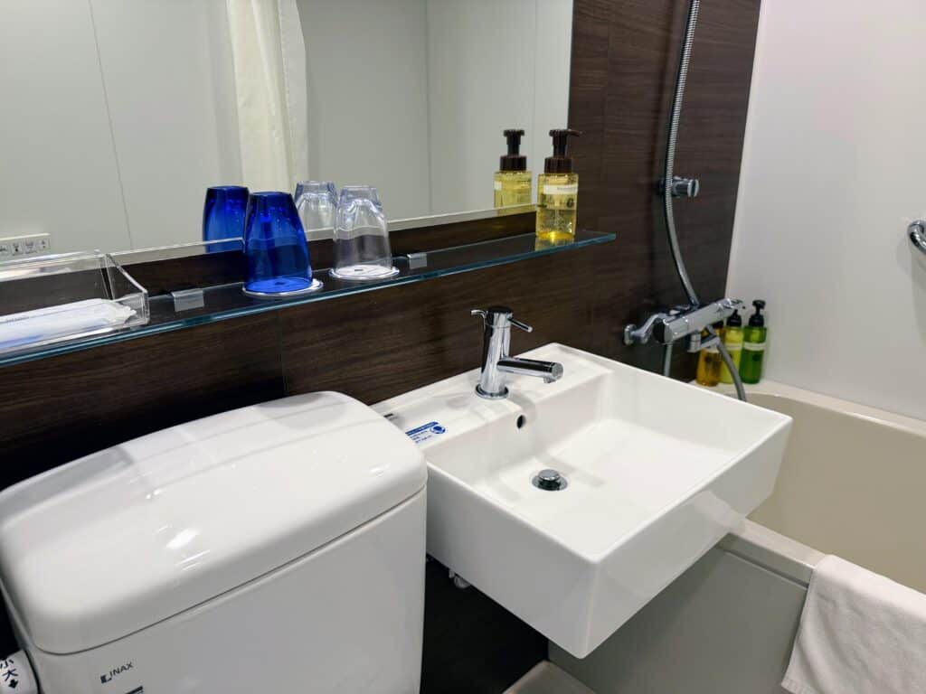 Bathroom with focus on sink and toiletries above the sink and in the shower. The shower has a bath as well.