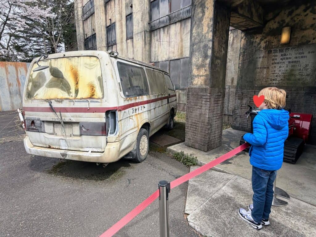 Boy looks at old van next to haunted hospital entrance at Fuji-Q Highland theme park in Japan.