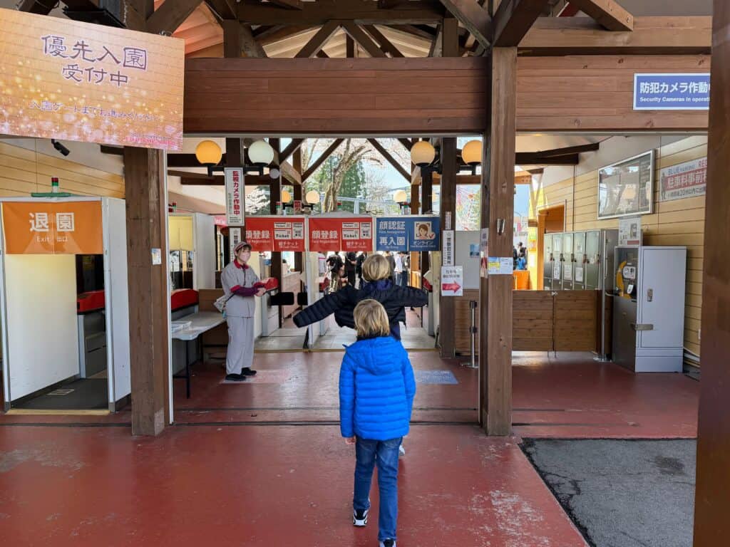 Boys walk toward the entrance gate at Fuji-Q Highland theme park in Japan. They are wearing coats. There is one worker at the entrance and no other guests.