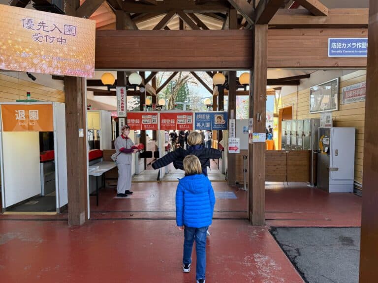 Boys walk toward the entrance gate at Fuji-Q Highland theme park in Japan. They are wearing coats. There is one worker at the entrance and no other guests.