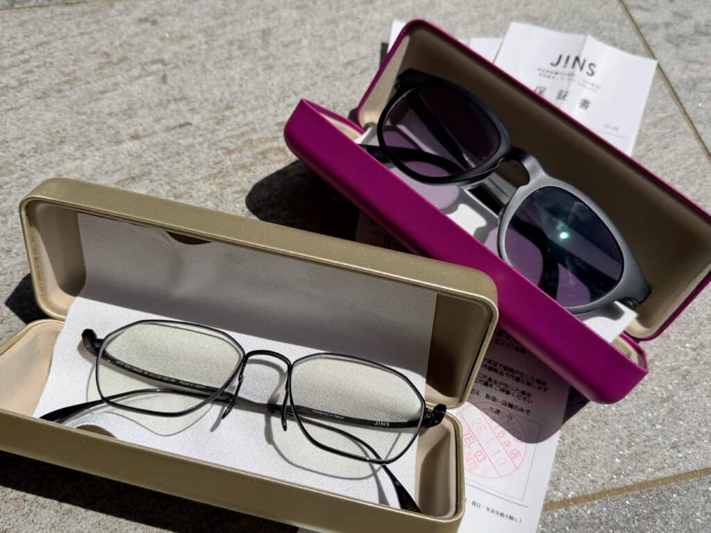 Two pairs of glasses in hard cases on a stone surface. The cases are on top of a receipt from JINS in Japan.