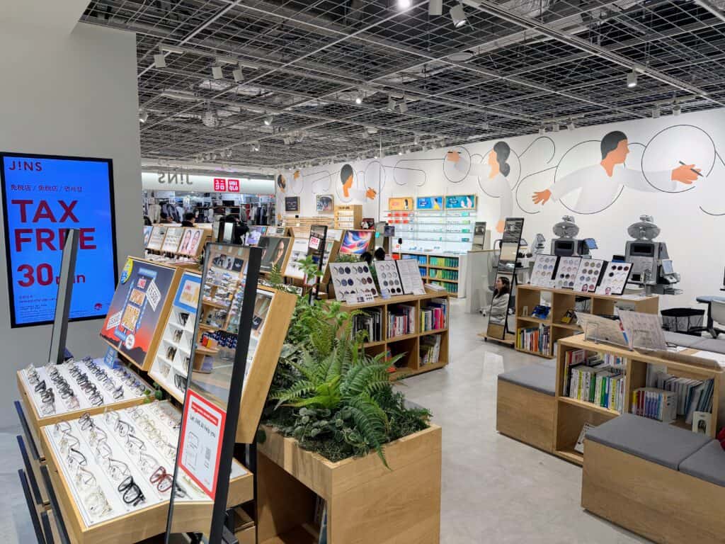 JINS glasses store in Tokyo, Japan. Displays of eyeglasses and underneath the displays are bookshelves full of books.