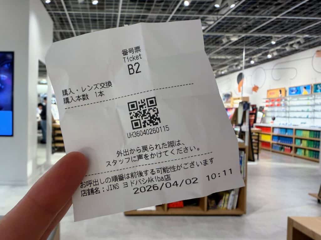 Hand holds up a ticket with a QR code and Japanese text inside the JINS glasses store in Tokyo's Yodobashi Akiba store.