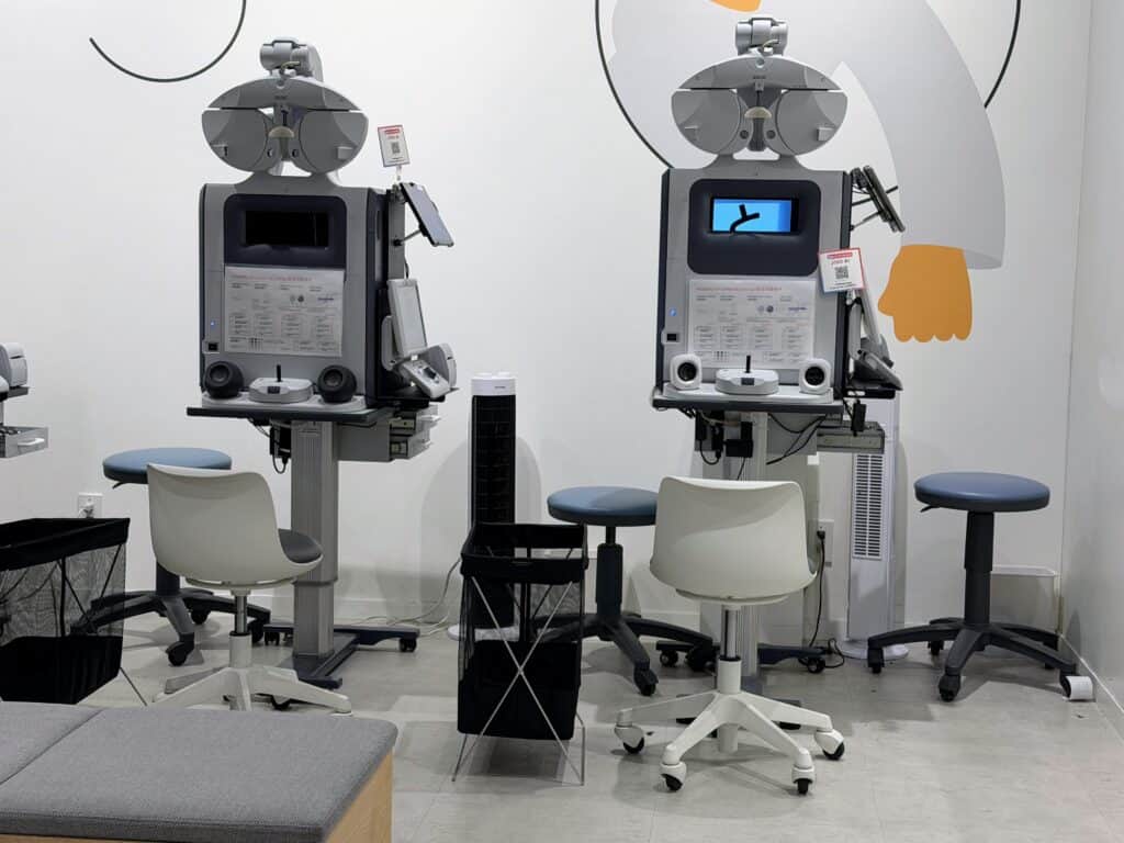Two grey machines with chairs in front of them. The machines are used to test eyes and give prescriptions. This is at a JINS store in Tokyo, Japan.