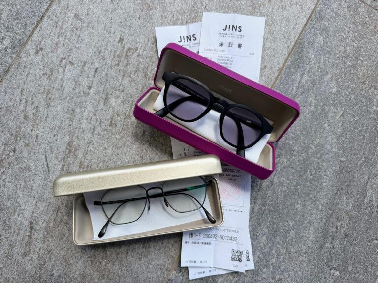 Two pairs of glasses in hard cases on a stone surface. The cases are on top of a receipt from JINS in Japan.