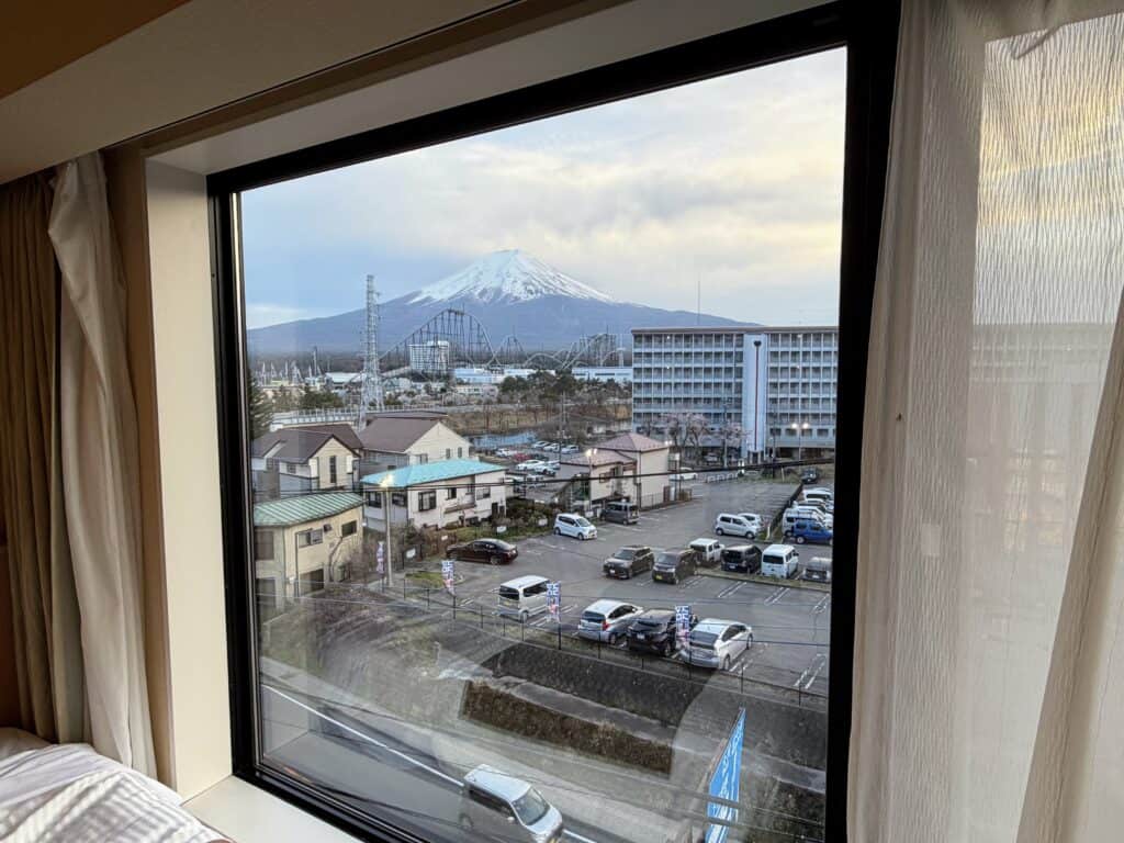 View from the window of a room at HOTEL MYSTAYS Fuji Onsen Resort. Mt. Fuji in background, along with roller coasters and buildings.