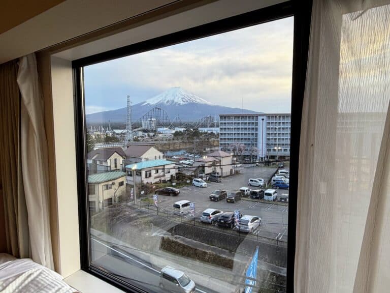 View from the window of a room at HOTEL MYSTAYS Fuji Onsen Resort. Mt. Fuji in background, along with roller coasters and buildings.