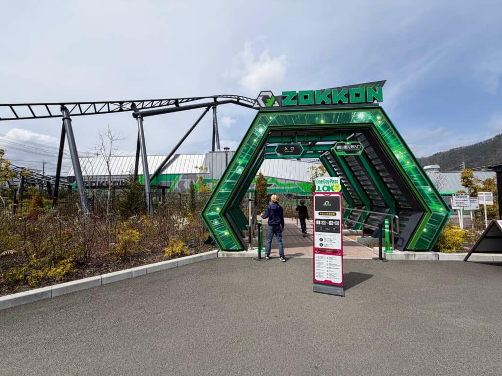 Two boys walk under green arch, which is the entrance to the Zokkon ride at Fuji-Q Highland in Japan.
