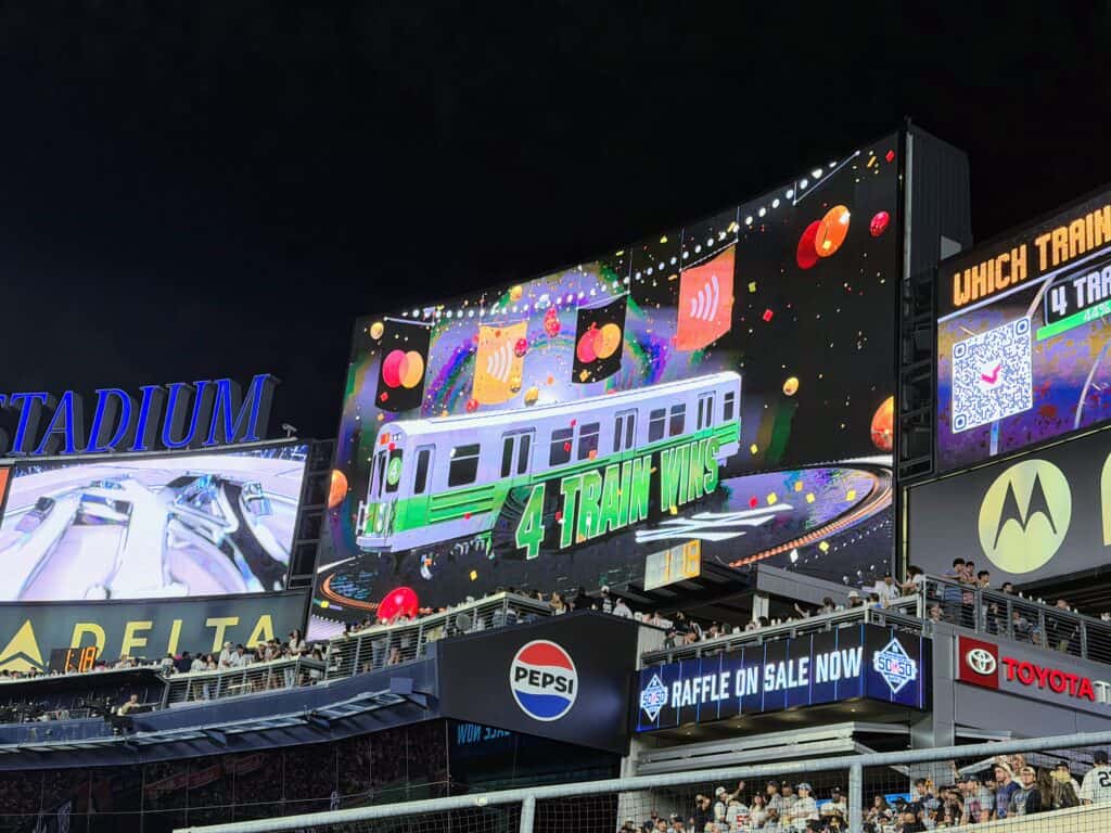 The digital screen at Yankee Stadium is lit up during a game with the subway race game, showing '4 Train Wins.'